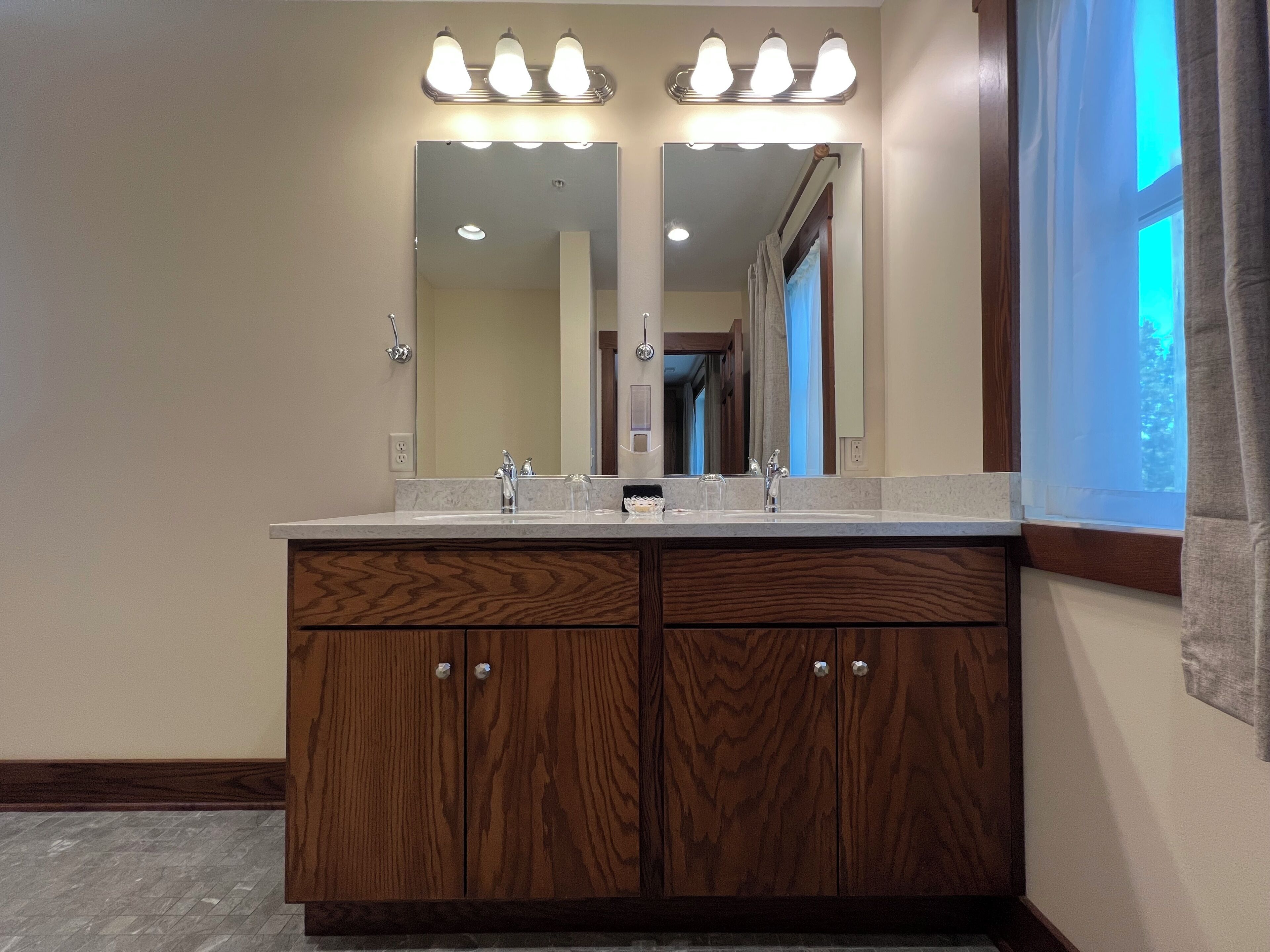 A bathroom with a vanity, two sinks, a mirror, and overhead lighting.