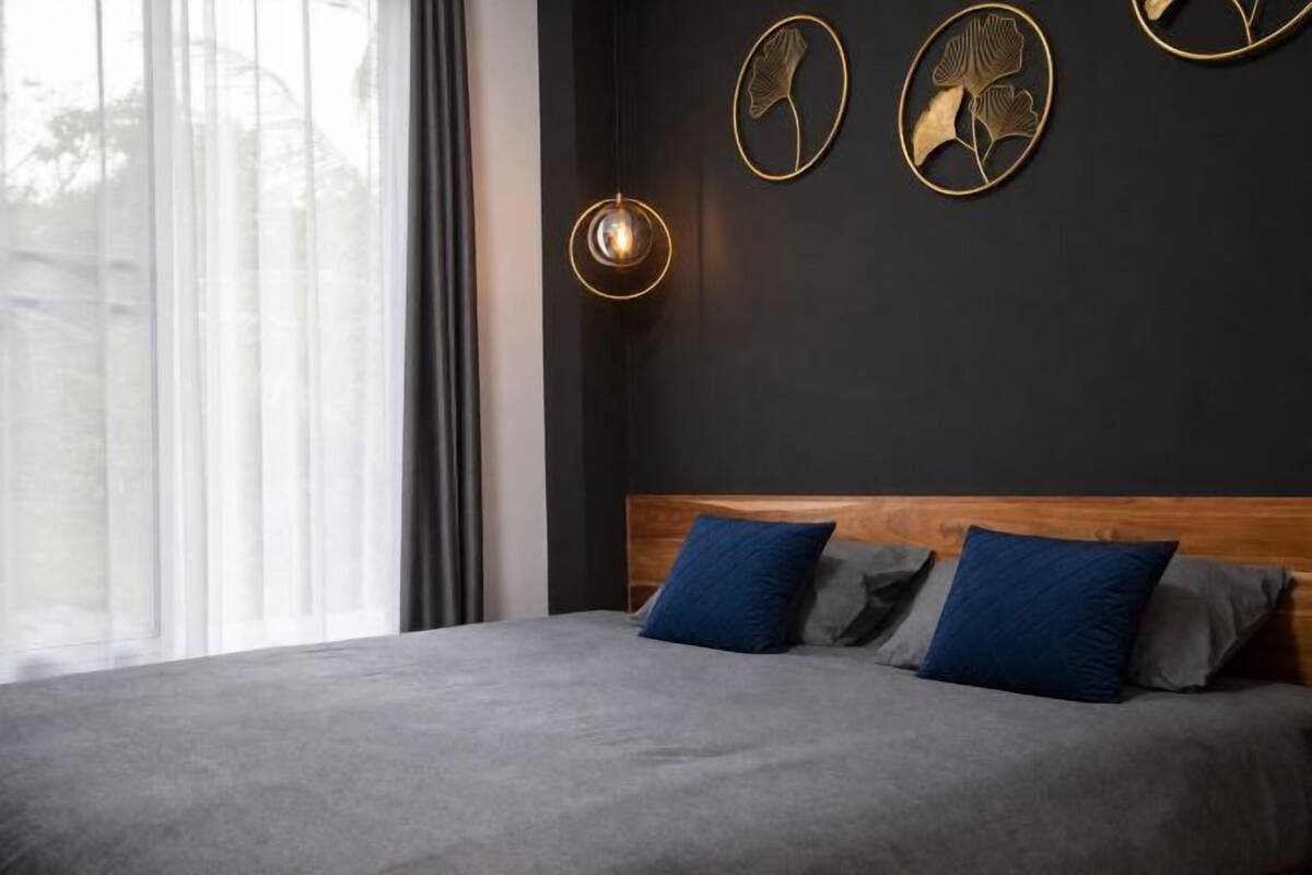 A modern bedroom with a large bed, dark walls, and decorative wall art.