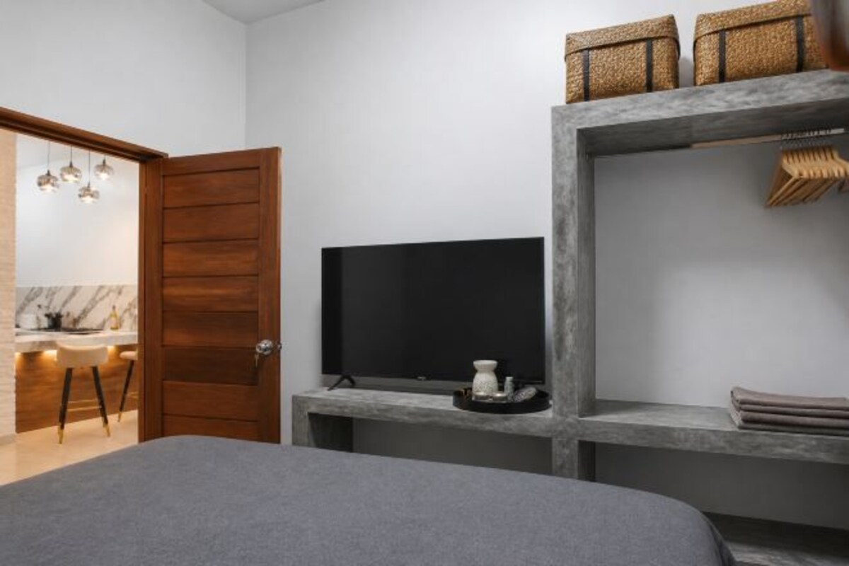 A modern bedroom with a bed, a TV, a wooden door, and a shelf with items.