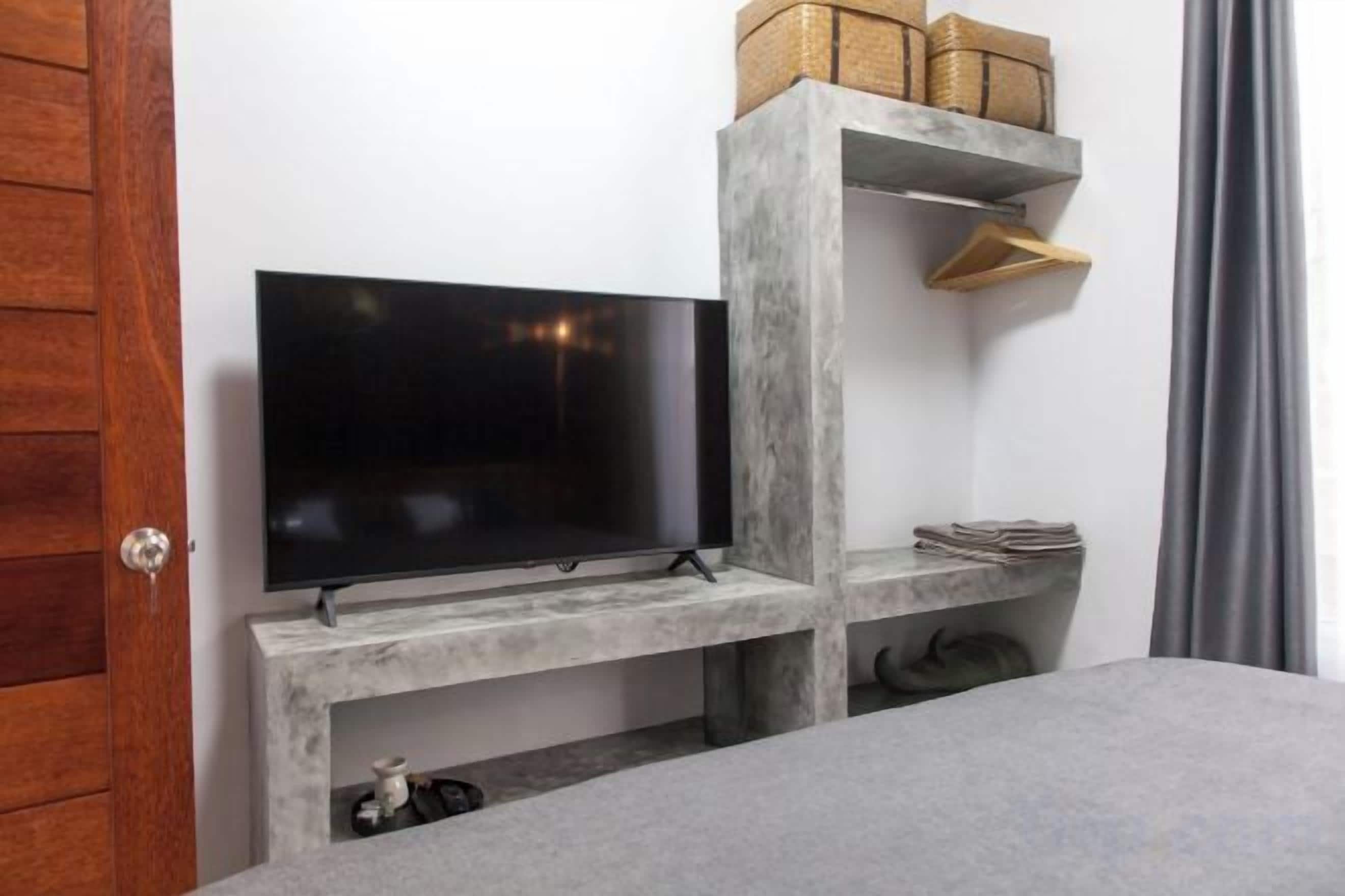 Un televisor sobre una estantería empotrada, una puerta y una ventana con cortinas.