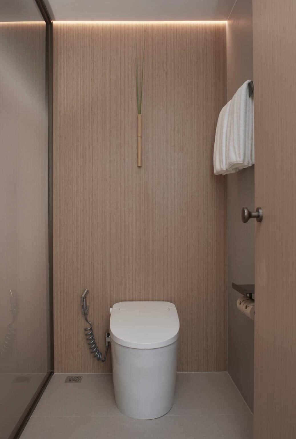 A modern bathroom with a white toilet, a bamboo brush, and a towel hanging on a rack.