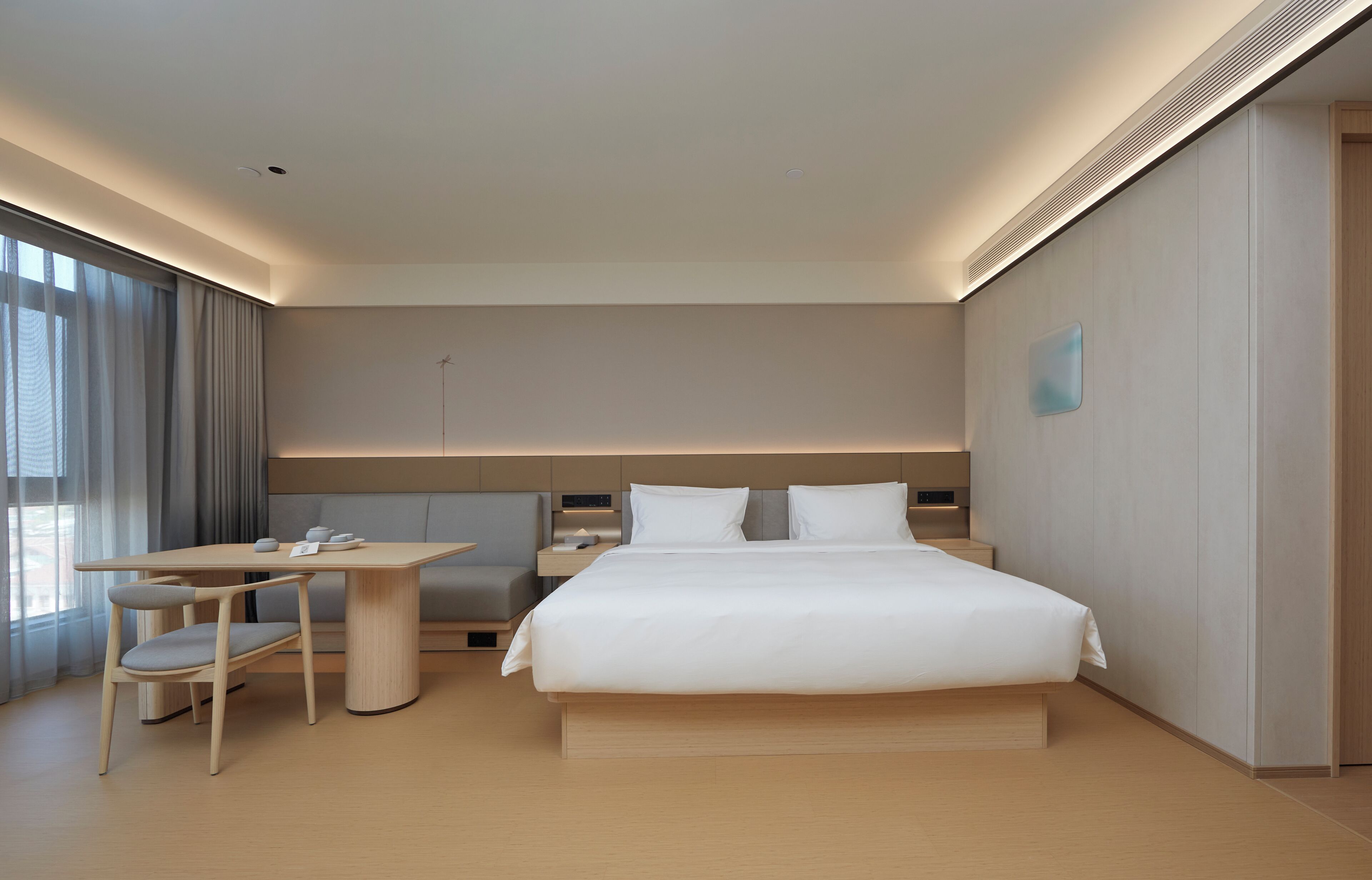 Quarto de hotel moderno com uma cama grande, uma escrivaninha com cadeira e vista para a cidade através de amplas janelas.