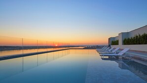 Una piscina infinita a la terrassa amb vistes al capvespre, gandules i una façana d'edifici moderna.