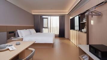 A modern hotel room with a large bed, a desk with a chair, a television, and a wardrobe.