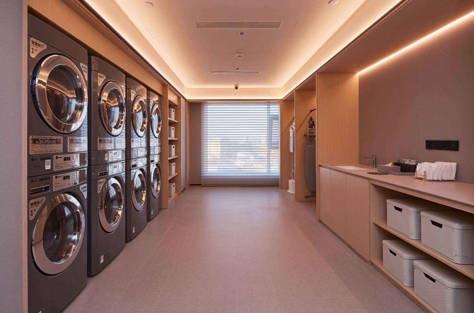 A laundry room with multiple washing machines, a sink, and storage bins.