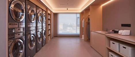 A laundry room with multiple washing machines, a sink, and storage bins.