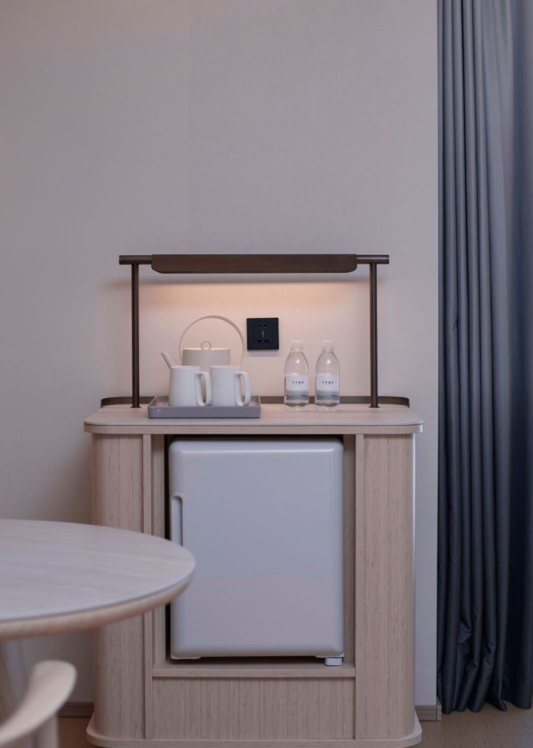 A compact kitchenette with a small refrigerator, a countertop with a kettle, cups, and water bottles.