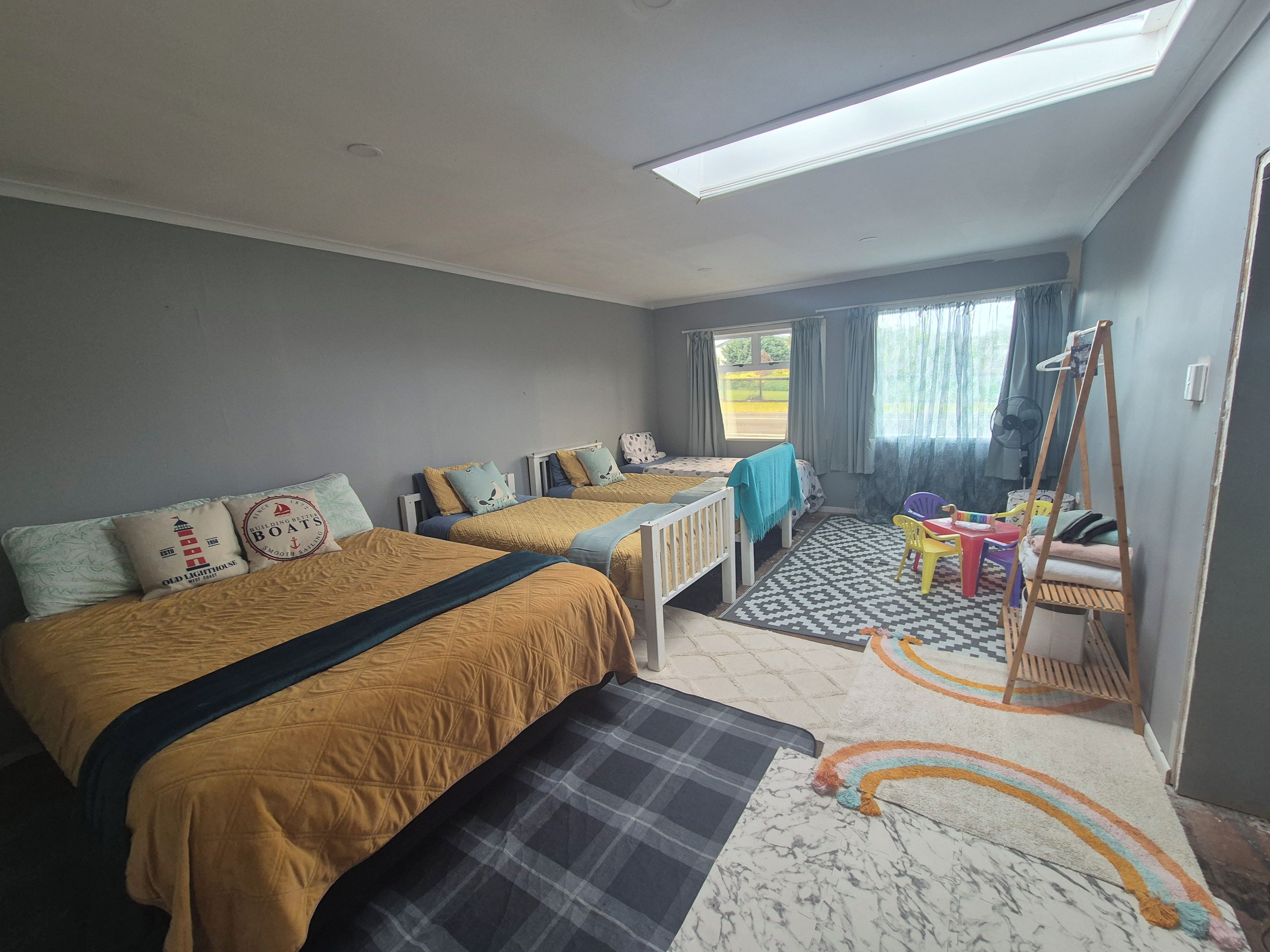 A hotel room with two beds, a small table, a chair, a fan, and a window with curtains.