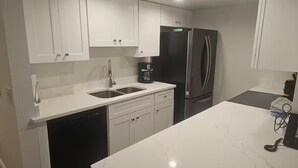 Una cocina moderna con armarios blancos, un refrigerador de acero inoxidable, una cafetera y un lavavajillas.
