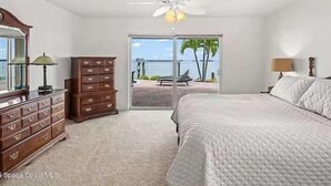 A bedroom with a bed, dresser, and a view of the ocean through a sliding door.