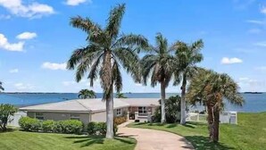 A beachfront property with a pathway leading to a house, surrounded by palm trees and a view of the ocean.
