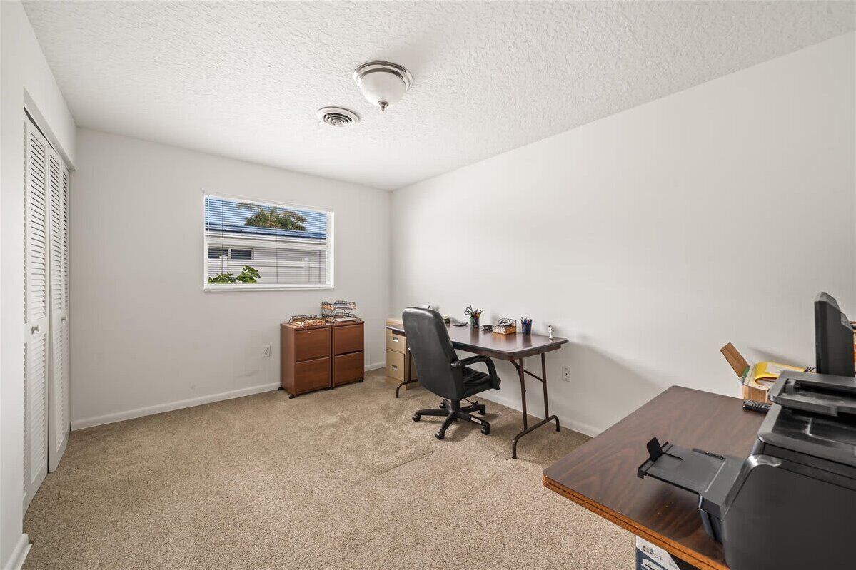 A small office space with a desk, chair, and filing cabinet. There is a window with blinds and a ceiling light.