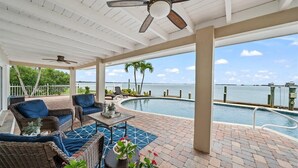 A covered outdoor area with wicker furniture, a pool, and a view of the ocean.