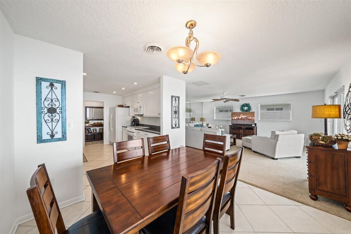 A spacious dining area with a wooden table and chairs, a kitchen in the background, and a living area with a white sofa and a lamp.