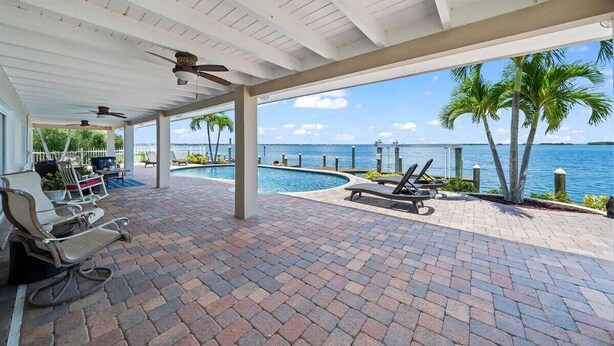 A covered outdoor area with a pool, lounge chairs, and a view of the ocean.
