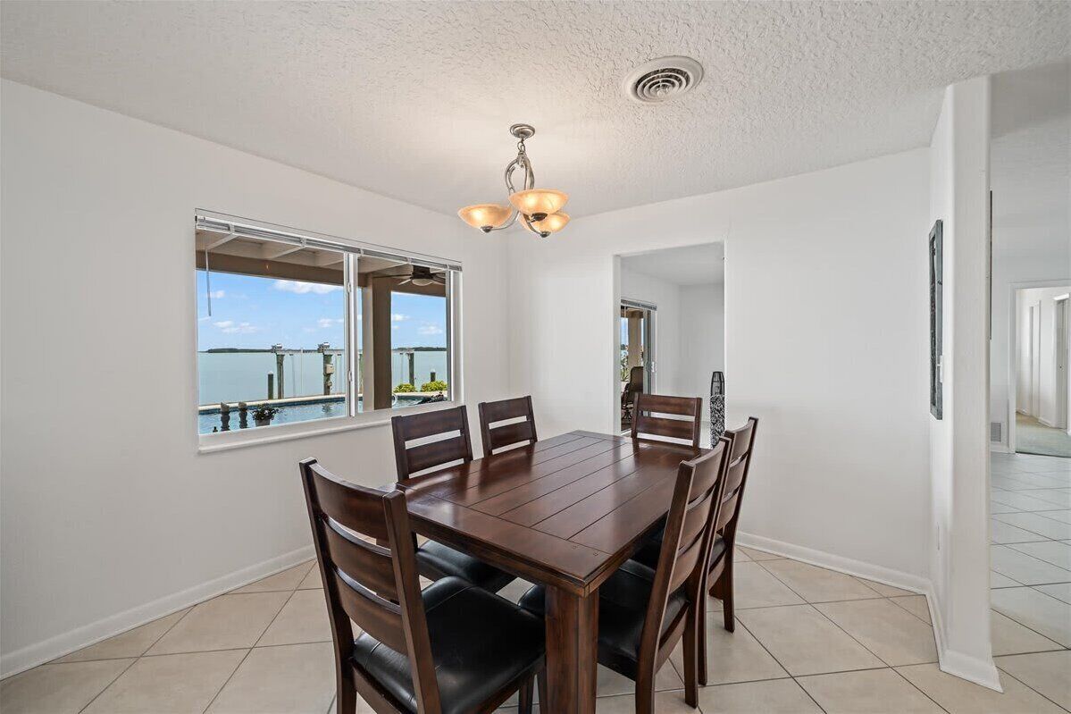 Un espace repas comprenant une grande table et des chaises, un luminaire au plafond et une fenêtre donnant sur la mer.