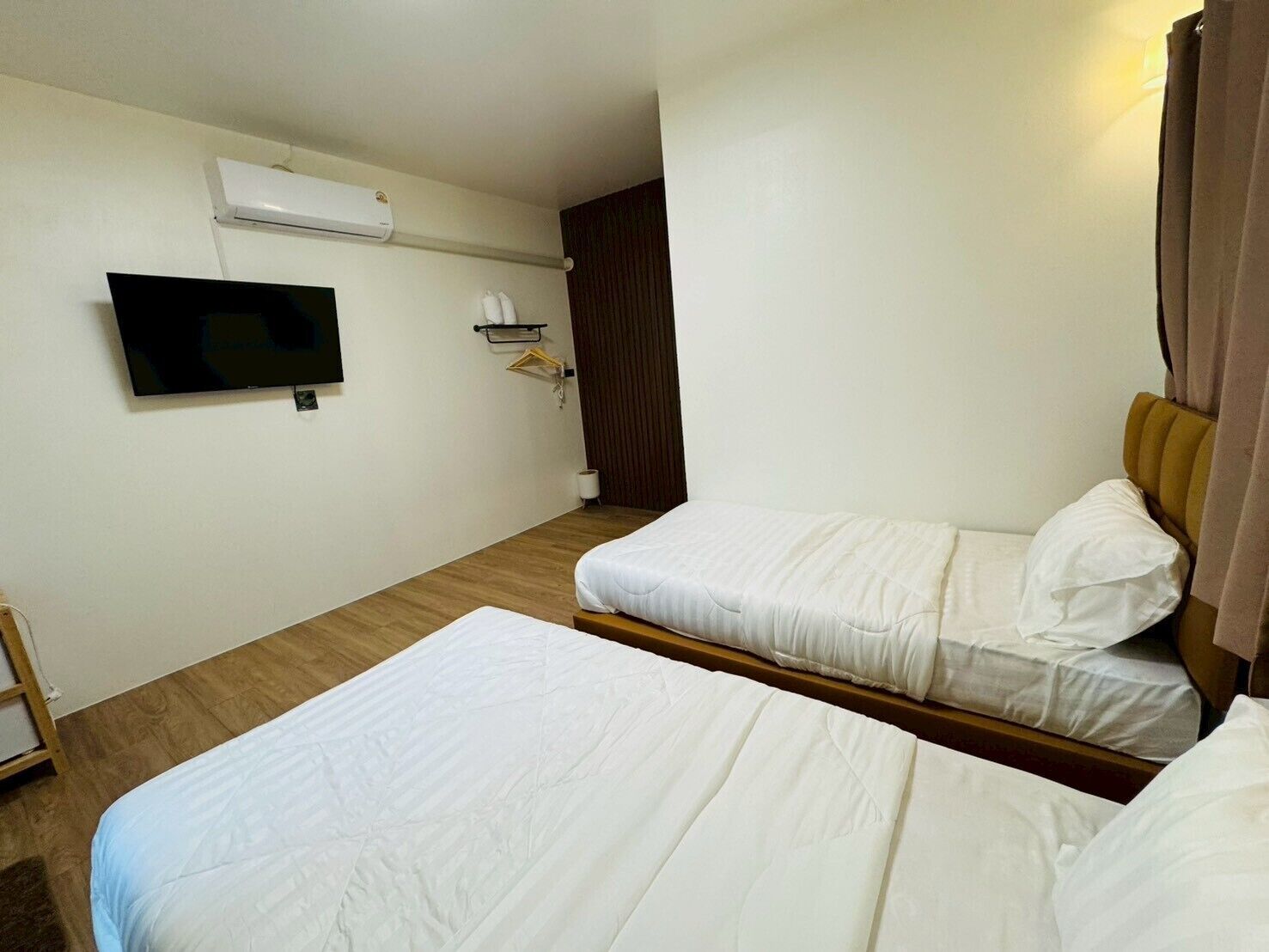 Una habitación de hotel con dos camas, un televisor montado en la pared y suelo de madera.