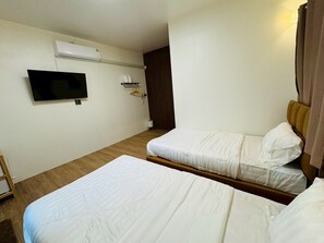 Una camera d'albergo con due letti, una TV fissata al muro e pavimento in legno.