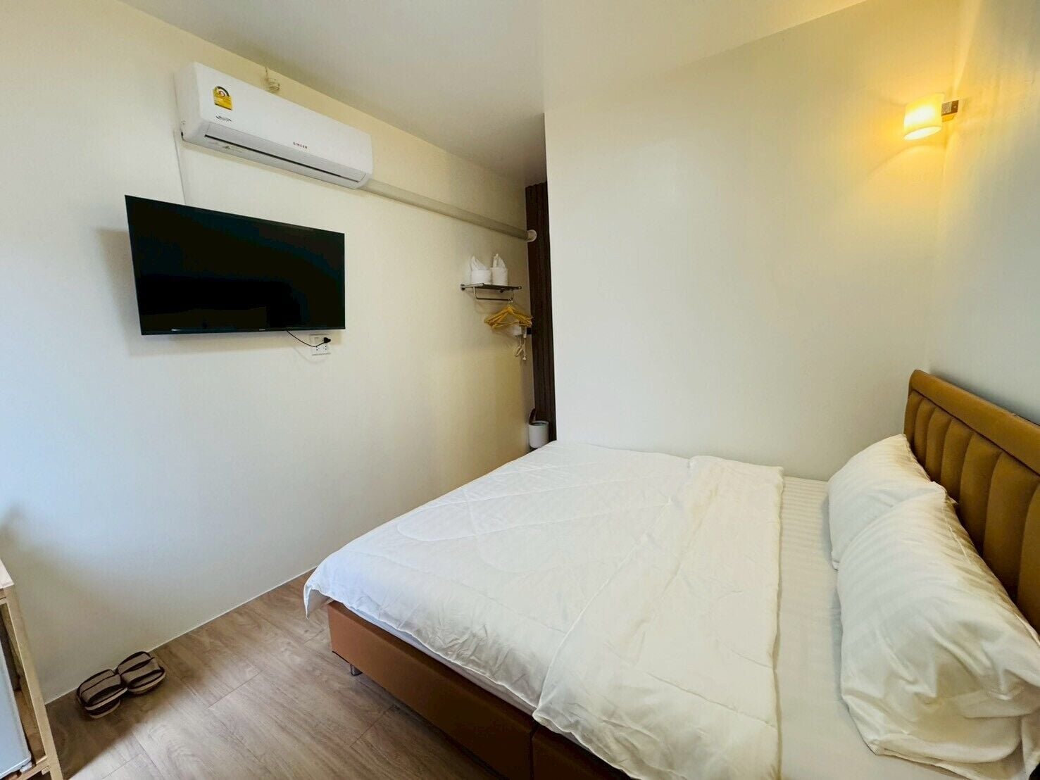 Quarto com cama, ar condicionado, televisão e luminária fixada na parede.