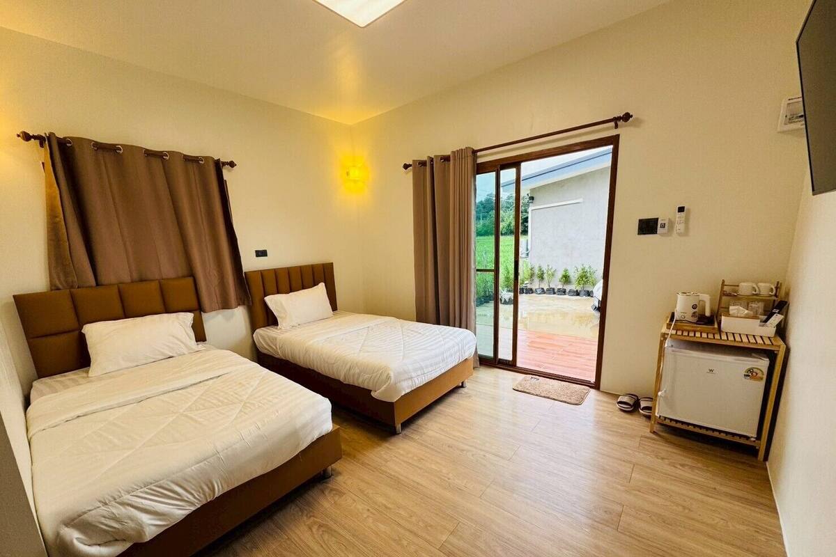 A hotel room with two beds, a small kitchenette, and a sliding glass door leading to an outdoor area.