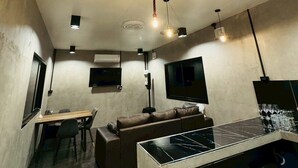 A compact living space with a dining area, a sofa, a TV mounted on the wall, and a kitchen area with a stove. - Wangnue Mountain View Resort&Hotel (Wang Nuea)