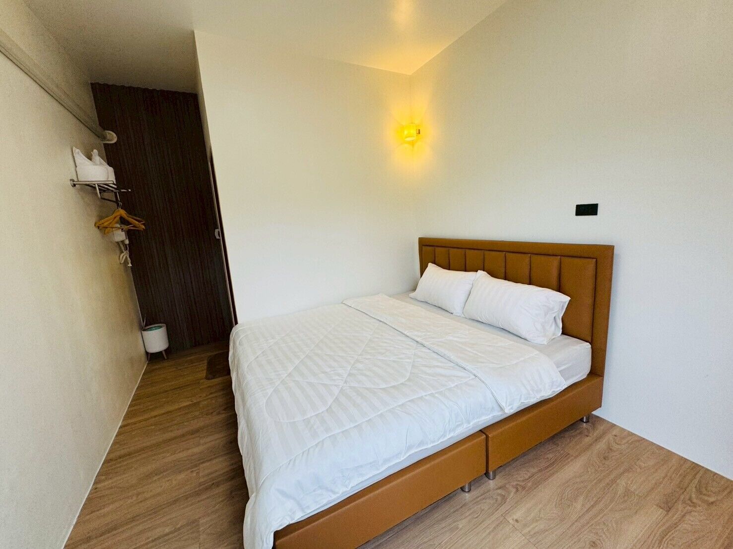 A bedroom with a bed, wooden headboard, and a wall-mounted light.
