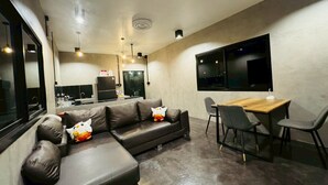 A modern living room with a sectional sofa, a dining area with a wooden table and chairs, and a kitchen in the background. - Wangnue Mountain View Resort&Hotel (Wang Nuea)