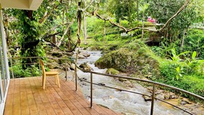 A wooden deck with a metal railing overlooking a flowing stream, surrounded by lush greenery. - Arb Pa Home And Cafe At Mae On (Mae On)