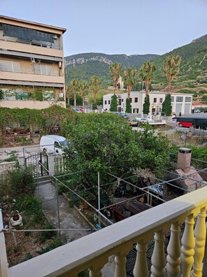 A residential area with a white van parked near a building with a balcony. There are palm trees and a mountainous background.