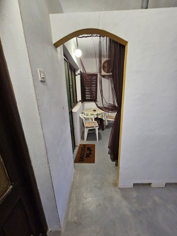 A narrow hallway with a small table and chair, a welcome mat, and a door leading to a room with a bed and a hanging net.