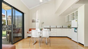 A modern kitchen with white cabinets, a dining area with white chairs, and a sliding glass door leading to an outdoor patio.