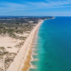 An aerial view of a coastal area with a long sandy beach and clear blue waters.