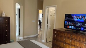 A hotel room with a bed, a dresser, a ceiling fan, and a TV displaying a streaming service interface. - Luxury 4-bedroom house with Pool and Entertainment Room Near Airport (Las Vegas)