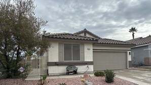 A residential house with a tiled roof, a garage, and a front yard with gravel and plants. - Luxury 4-bedroom house with Pool and Entertainment Room Near Airport (Las Vegas)