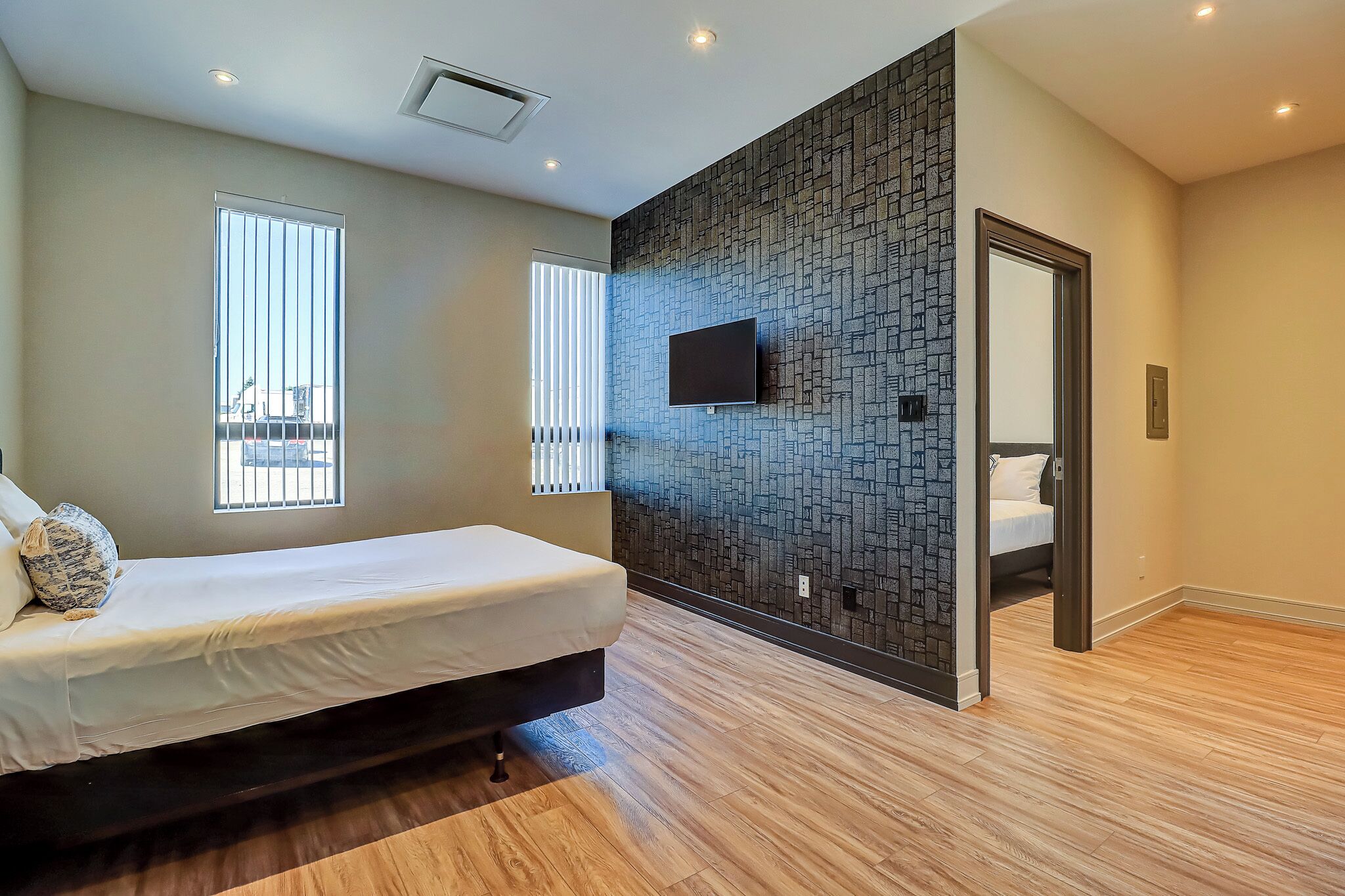 Un dormitorio moderno con una cama, un televisor montado en la pared y suelo de madera.