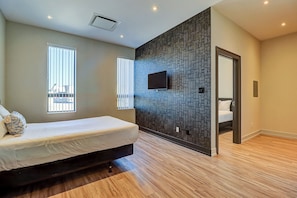 A modern bedroom with a bed, a TV mounted on the wall, and a wooden floor. - Dream Suites Near YYZ Airport (Mississauga)