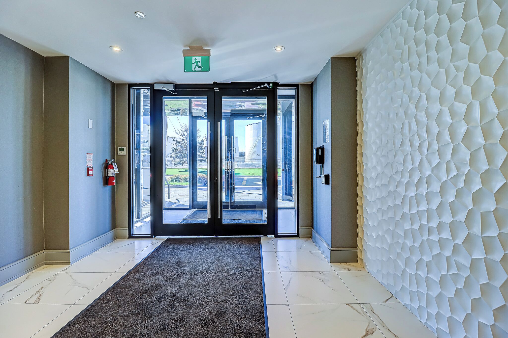 Un moderno vestíbulo de hotel con piso de mármol, alfombra gris, puerta de vidrio de entrada y pared blanca con textura.