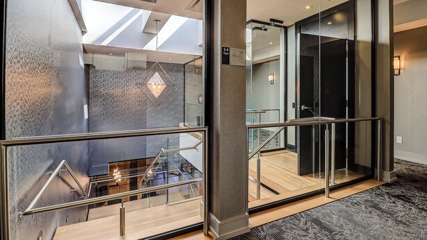 A modern hotel interior with a glass elevator, a staircase with metal railings, and a skylight. - Dream Suites Near YYZ Airport (Mississauga)