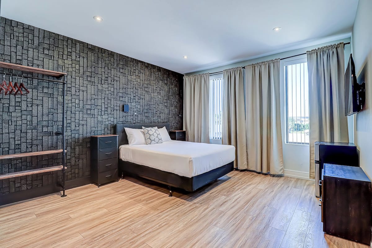 Camera moderna con parete effetto pietra, pavimento in legno, un letto con testiera, una televisione e una finestra con tende.