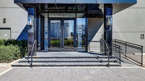 A modern building entrance with glass doors, a staircase, and a metal railing. - Dream Suites Near YYZ Airport (Mississauga)