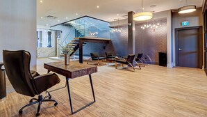 A modern lobby with a wooden floor, a reception desk, leather chairs, a staircase, and a glass railing. - Dream Suites Near YYZ Airport (Mississauga)
