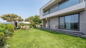 A modern two-story house with a well-maintained lawn, outdoor furniture, and a large window overlooking the garden. - Ganghwa Noeuldamechae Private Pension (Incheon)
