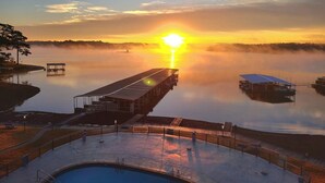 Un espace piscine avec une jetée s’avançant dans l’eau, entouré d’un lac paisible au coucher du soleil.