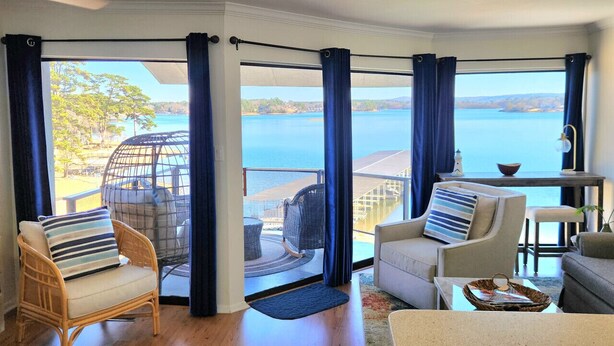 Un salon avec vue sur la mer, des fauteuils en osier, un canapé et une petite table.