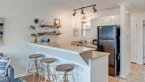 Une cuisine moderne dotée d’un îlot central, de tabourets de bar, d’un réfrigérateur et d’un luminaire suspendu.