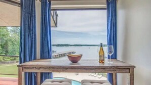 Une table avec un saladier, une bouteille de vin et un verre, donnant sur une piscine et une jetée.