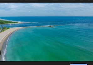 Ein Küstenstrand mit klarem türkisblauem Wasser, einem Sandufer und einem Wellenbrecher.