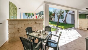 A patio with a table set for four, surrounded by chairs, and a view of a garden and buildings in the background. - Borgo Primizia B5 Pool And Sea, Otranto, Italy (Otranto)