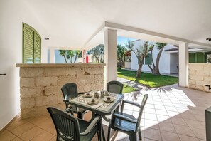 Eine Terrasse mit einem Tisch für vier Personen, umgeben von Stühlen, mit Blick auf einen Garten und Gebäude im Hintergrund.