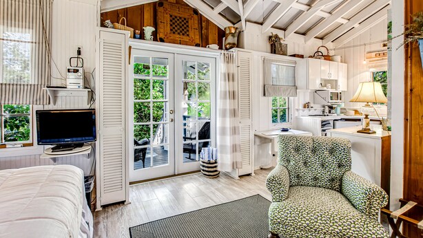 Una habitación acogedora con cama, escritorio, silla y televisión. Hay puertas abiertas que dan a un espacio exterior con mesa y sillas.